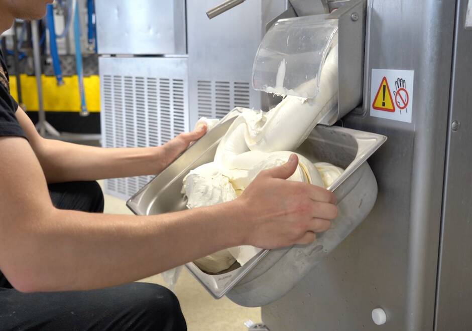 Une personne qui récolte dans un bac de la masse alimentaire produite par une machine